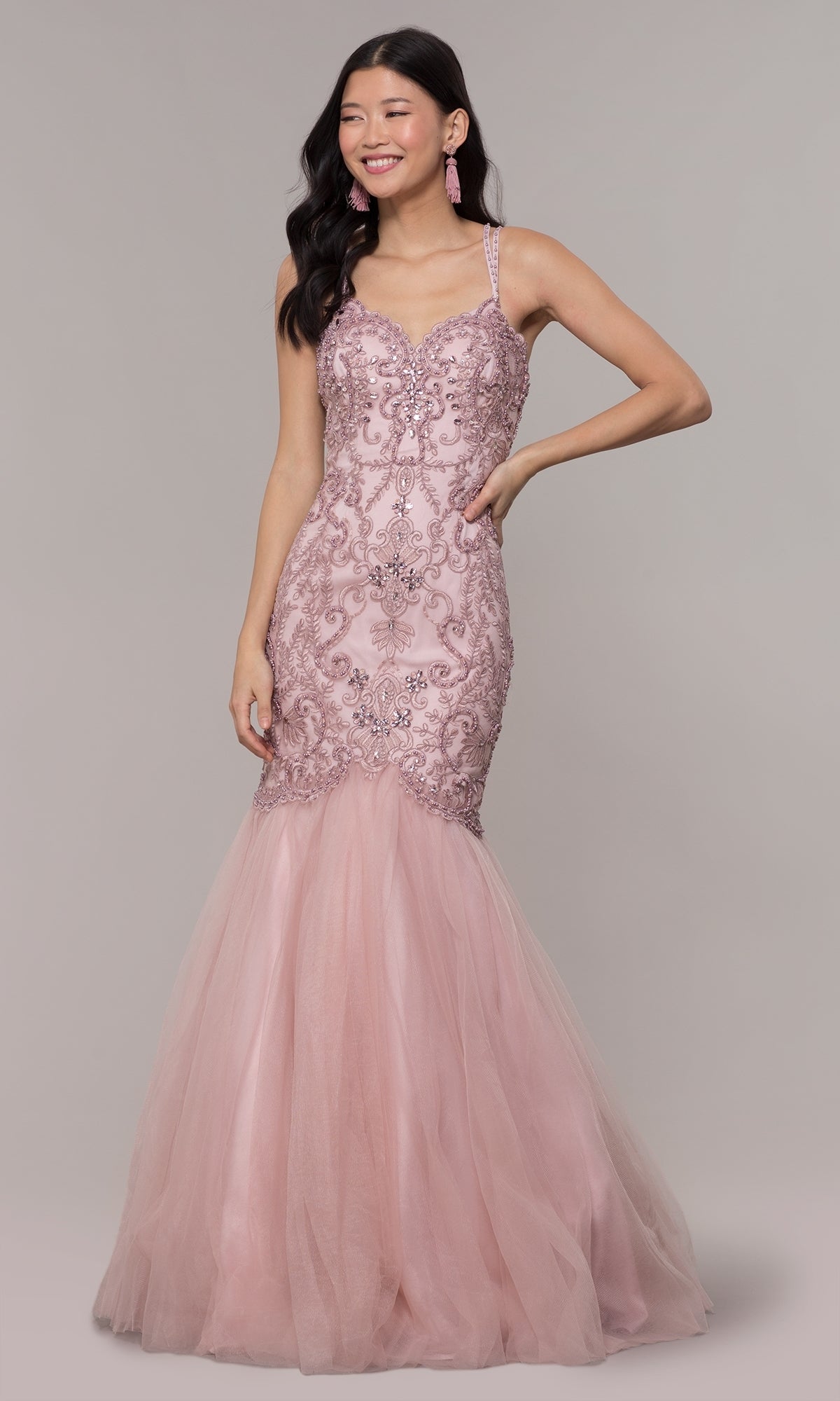 A woman stands and smiles against a plain background in the Embroidered Tight Sweetheart Mermaid Prom Dress 8352, a fitted light pink gown featuring elegant beading and embroidery.